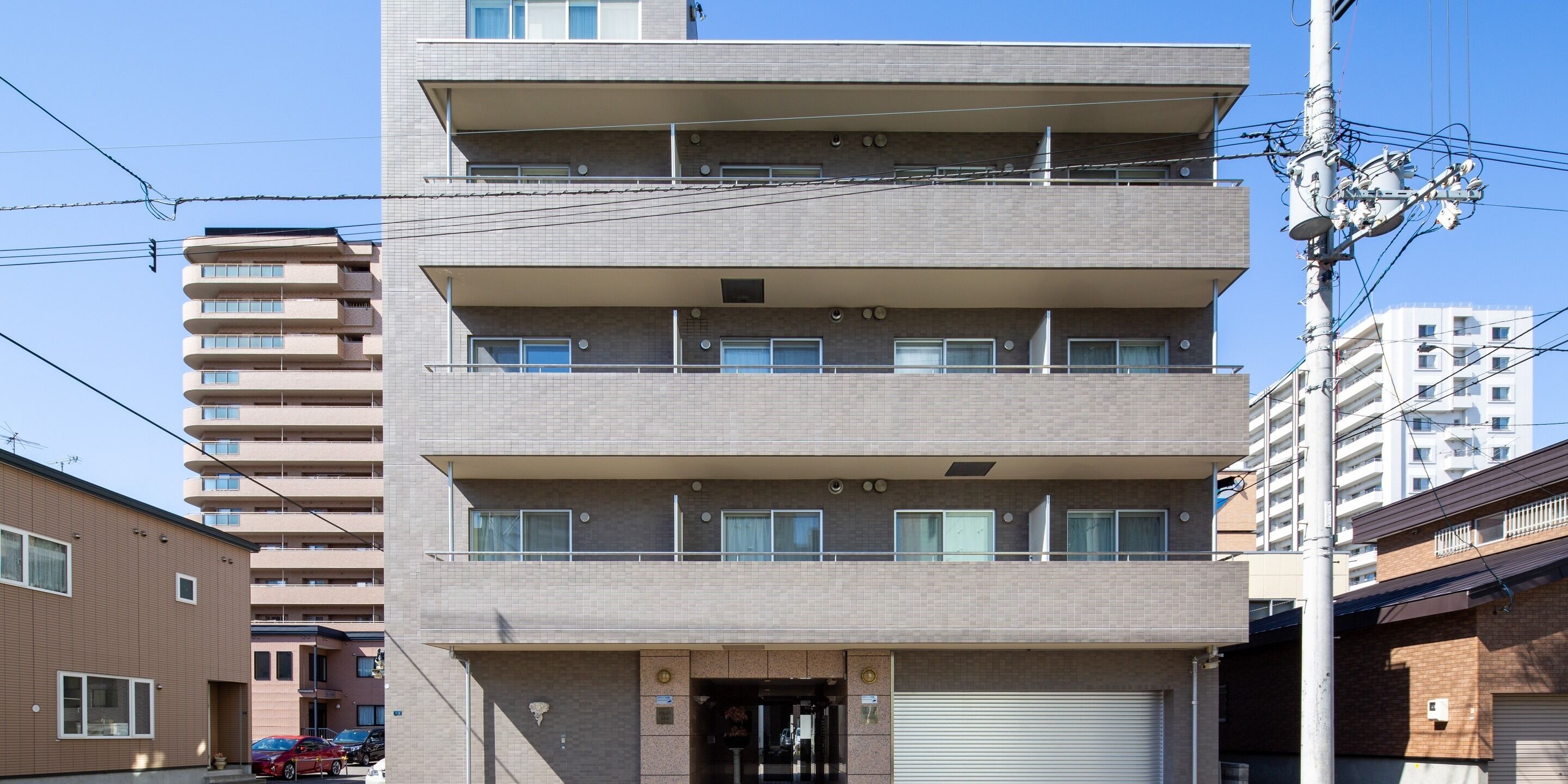 A multi-story building with a flat facade, balconies on each floor, and a garage door at the entrance.