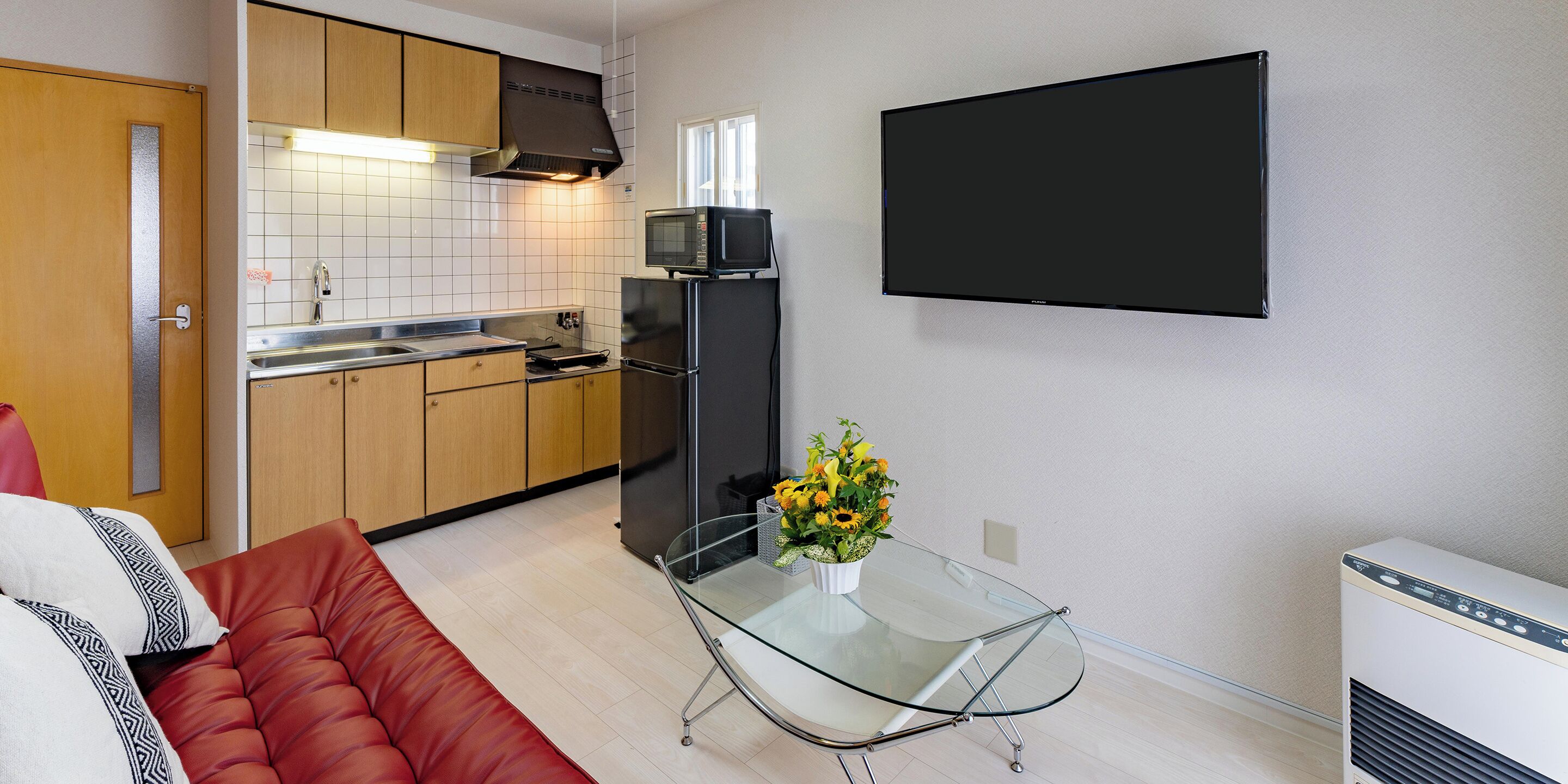 A compact kitchen with a microwave, refrigerator, and a glass table with a flower vase.