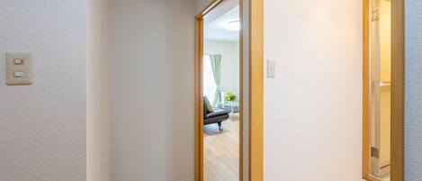 A hallway with a door leading to a room, a light switch, and a visible part of a bed with a green pillow.