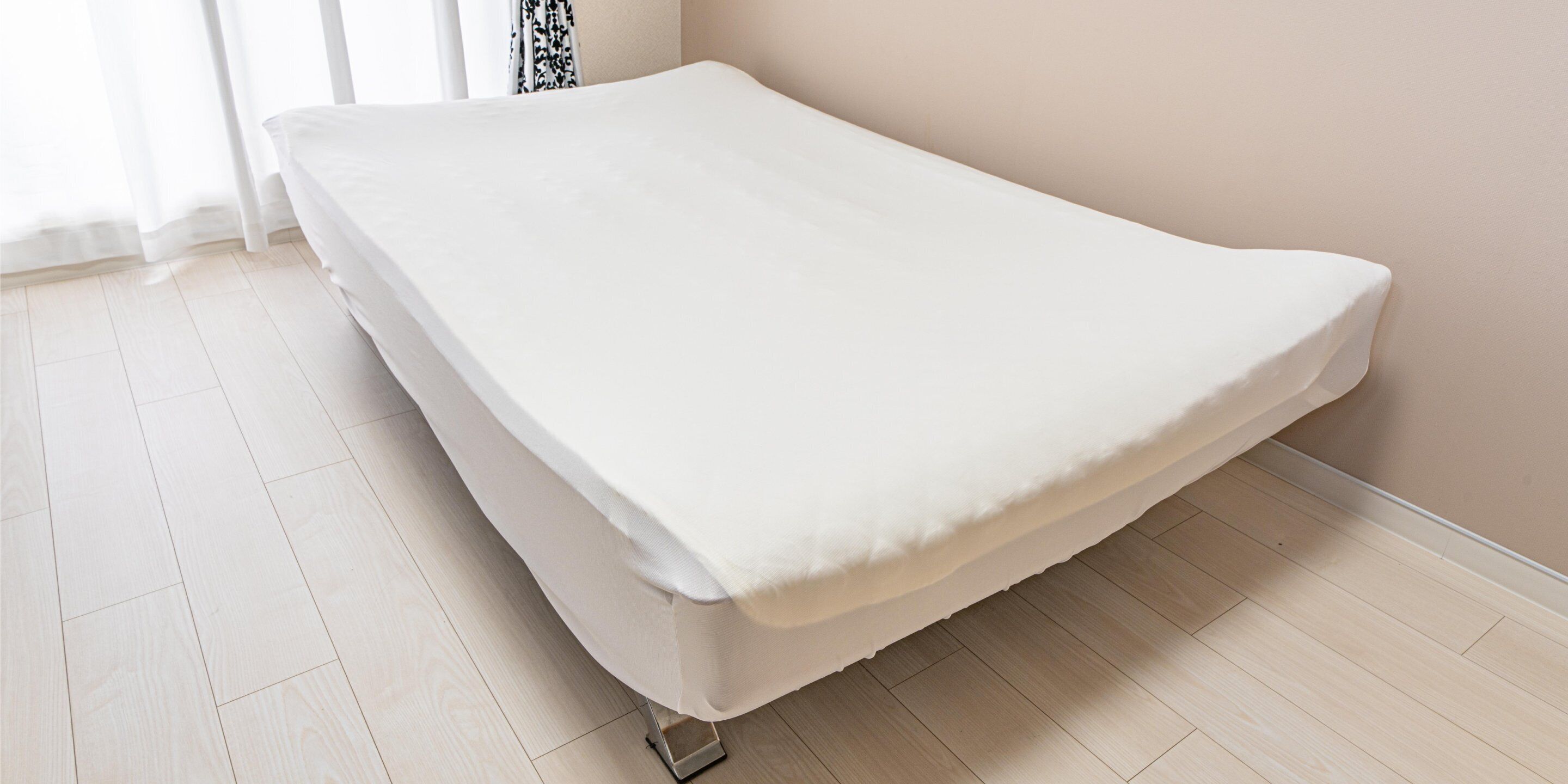 A single bed in a room with light wooden flooring and a plain wall.