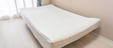 A single bed in a room with light wooden flooring and a plain wall.