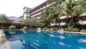 A swimming pool with clear blue water, surrounded by palm trees and a building with multiple balconies. - Eastpana Hotel (Si Racha)