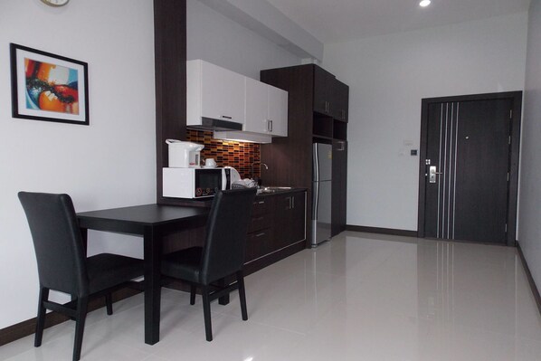 A modern kitchen with dark cabinetry, a white countertop, a stainless steel refrigerator, and a microwave. - Eastpana Hotel (Si Racha)