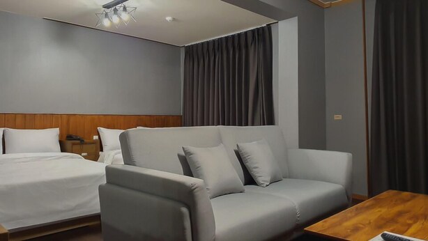A hotel room with a grey sofa, a wooden coffee table, and a bed with white linens. - Pure Stay (Jeju City)
