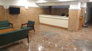 A reception area with a reception desk, a television mounted on the wall, and a seating area with green upholstered chairs and a sofa. - Pure Stay (Jeju City)