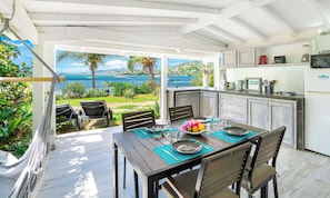 A dining area with a view of the ocean, a kitchen with white cabinets, and a hammock by the window. - 💖💖💖studio nature reserve pool/beach/kayak included (st martin)