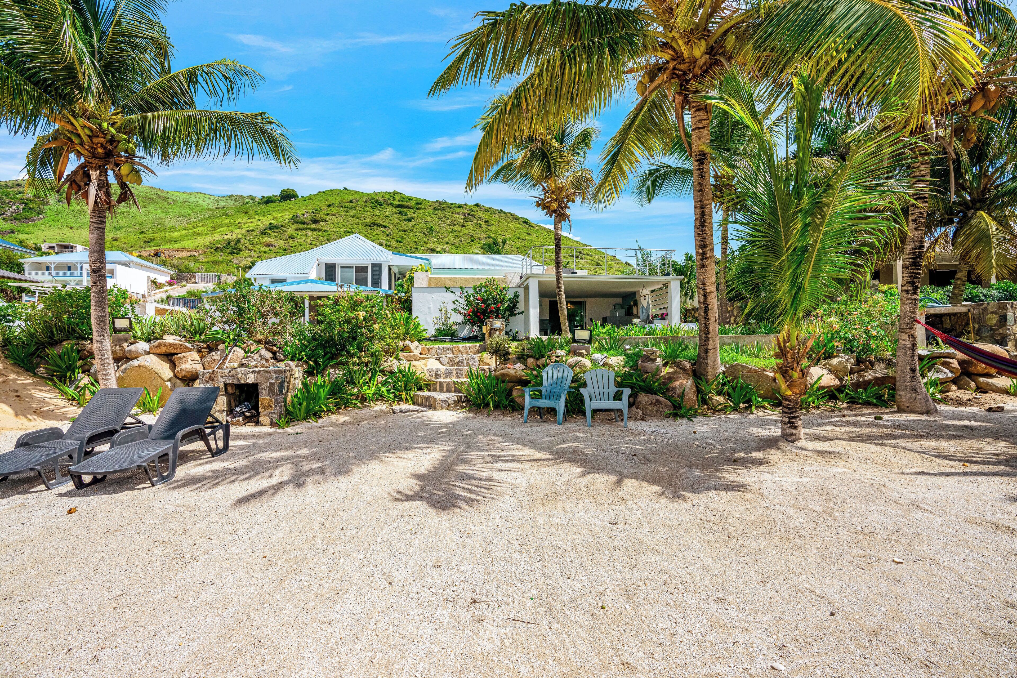 Une propriété située en bord de mer, dotée d’une terrasse sablonneuse, de chaises longues et d’un petit espace piscine.