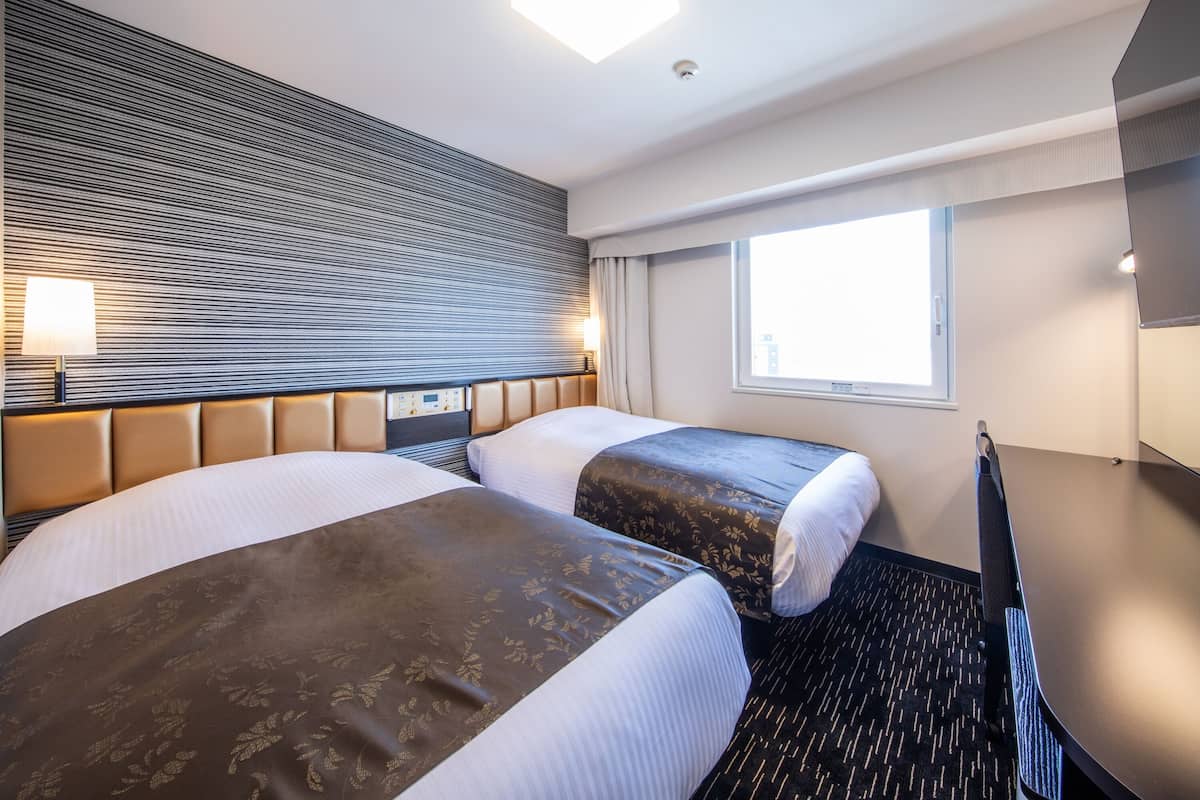 A hotel room with two beds, a large window, a flat-screen TV, and a desk.