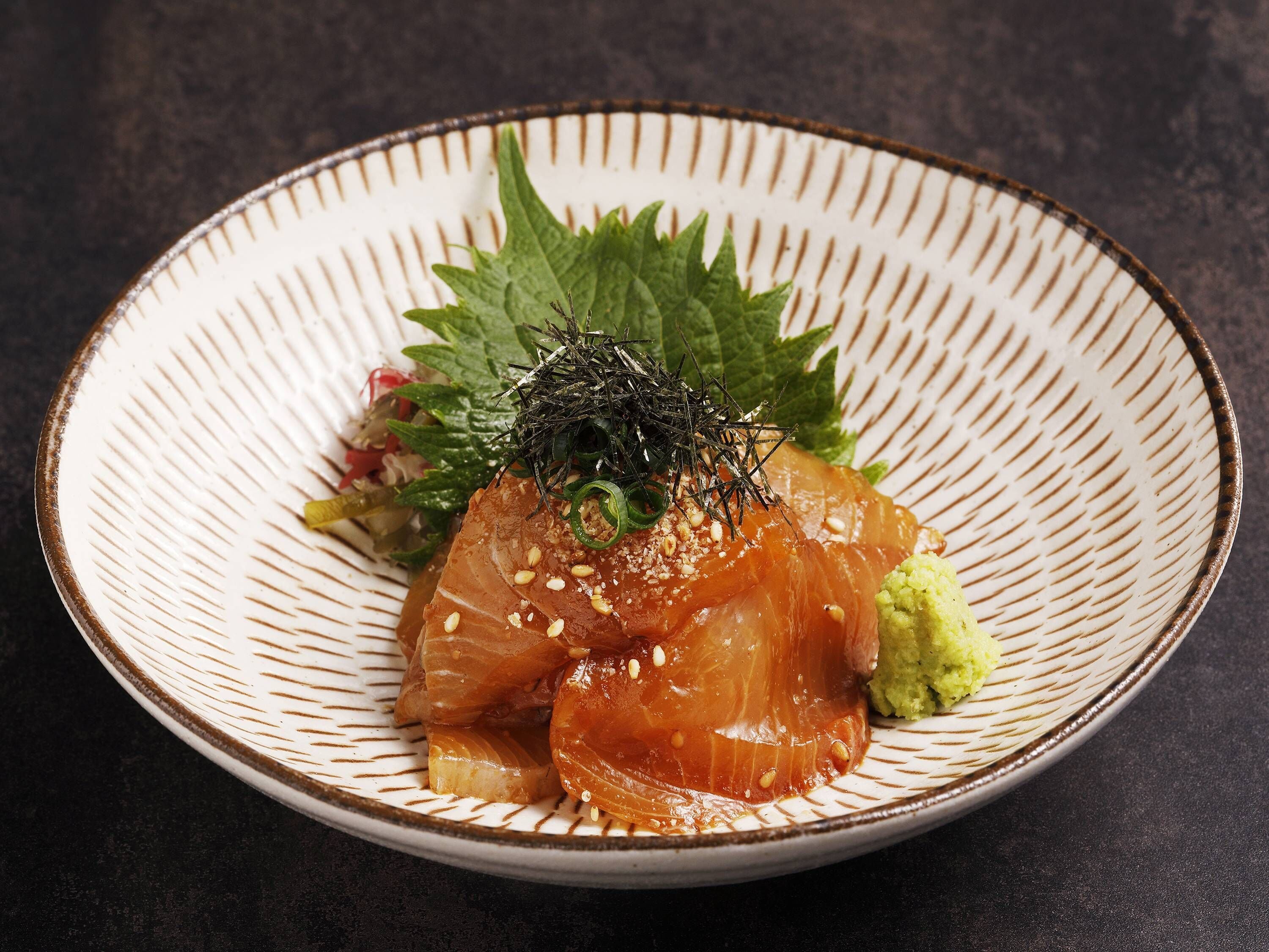 A plate of sushi with salmon, avocado, and garnishes on a textured ceramic plate.
