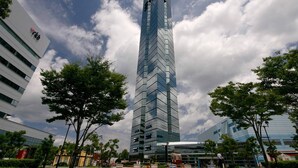Un rascacielos moderno con un diseño en zigzag distintivo, rodeado de árboles y otros edificios.