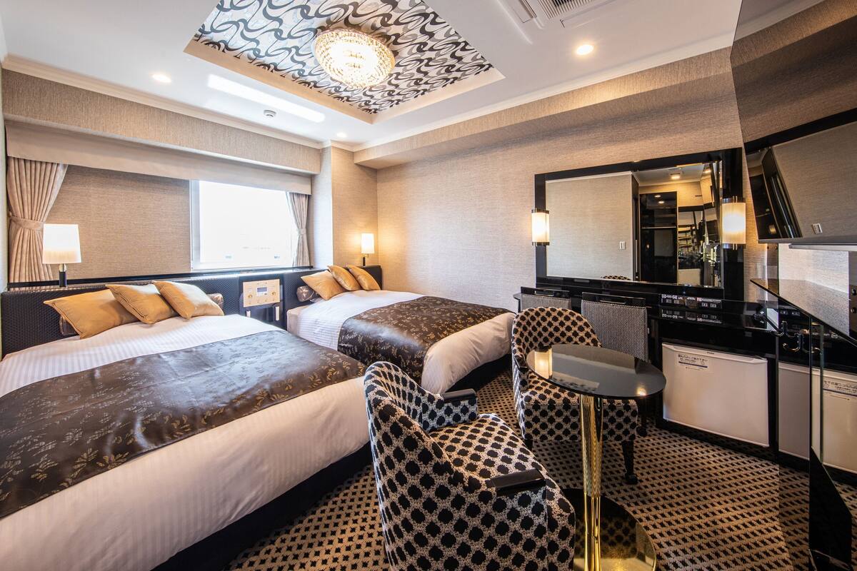 A hotel room with two beds, a desk, a chair, a mirror, and a patterned ceiling.
