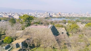 A historical site with stone structures and a park area, surrounded by a cityscape and a body of water in the background.