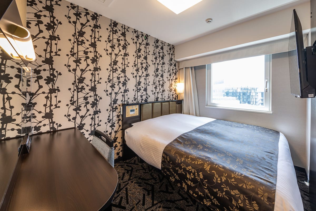 A hotel room with a bed, a desk, a chair, a TV, and a window with a city view.