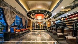 Un vestíbulo de hotel con suelo de mármol, zonas de estar, un mostrador de recepción y vistas a la ciudad.