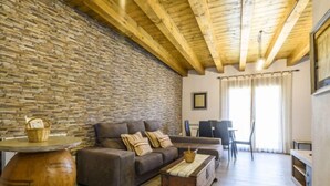 A living room with a stone wall, wooden ceiling beams, a brown sofa, a wooden coffee table, and a large vase.