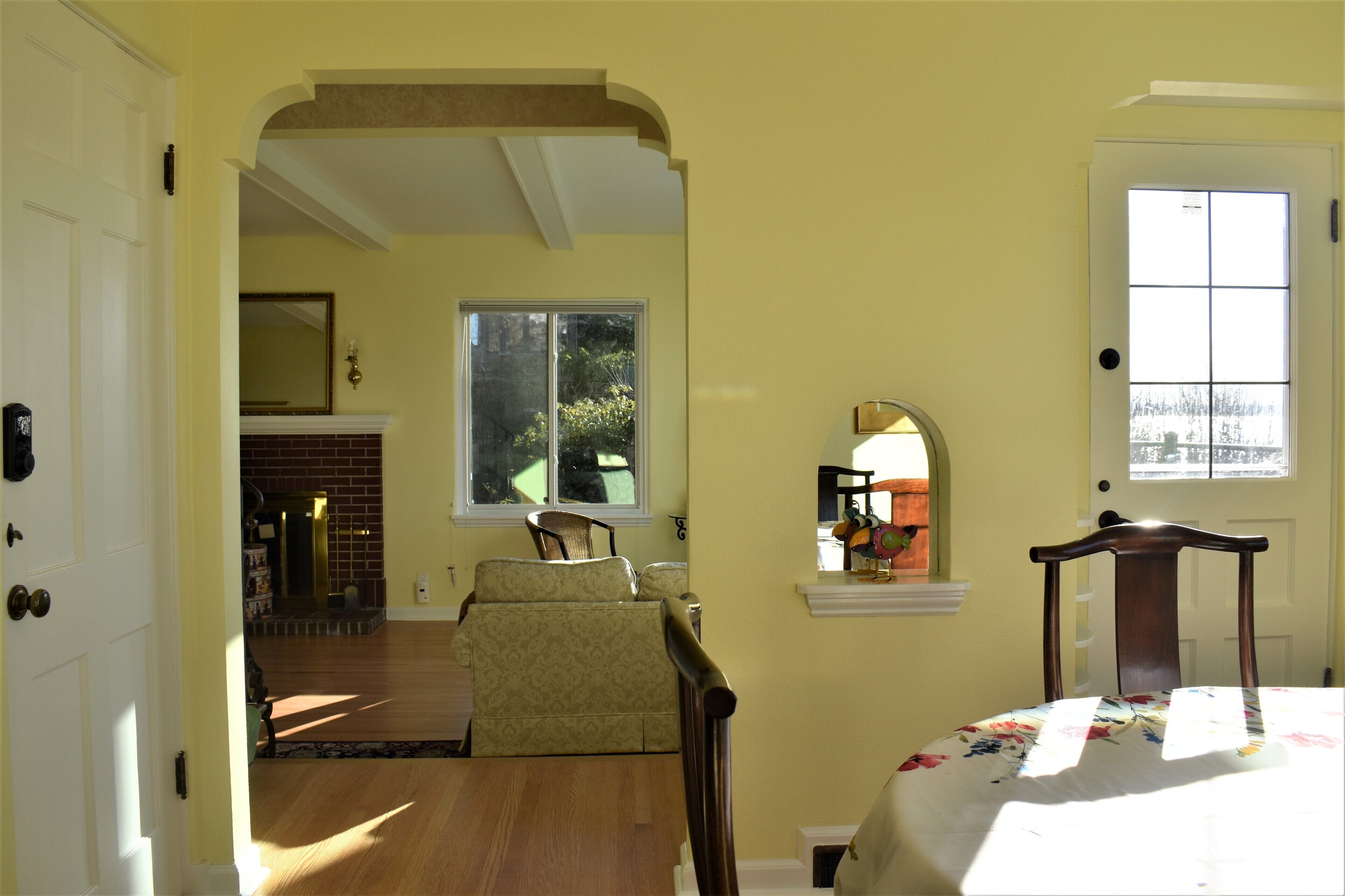 A room with a wooden floor, a bed with a floral bedspread, a chair, and a window with a view of greenery.