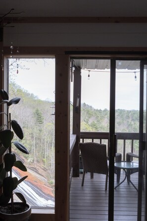A wooden deck with a chair and table, a potted plant, and a view of a forested hillside.