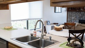 Une cuisine dotée de deux éviers, de meubles en bois, d’une cheminée en pierre et d’un coin repas avec une chaise et une table.