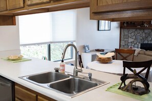 A kitchen with two sinks, wooden cabinets, a stone fireplace, and a dining area with a chair and table.