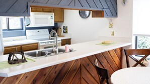 Une cuisine moderne avec un mur d’accent en bois, un plan de travail blanc, un évier en acier inoxydable et un four à micro-ondes.