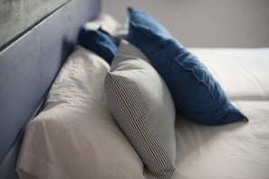 A bed with white bedding and three pillows, one striped and two solid blue. - Soul Surfer (La Oliva)