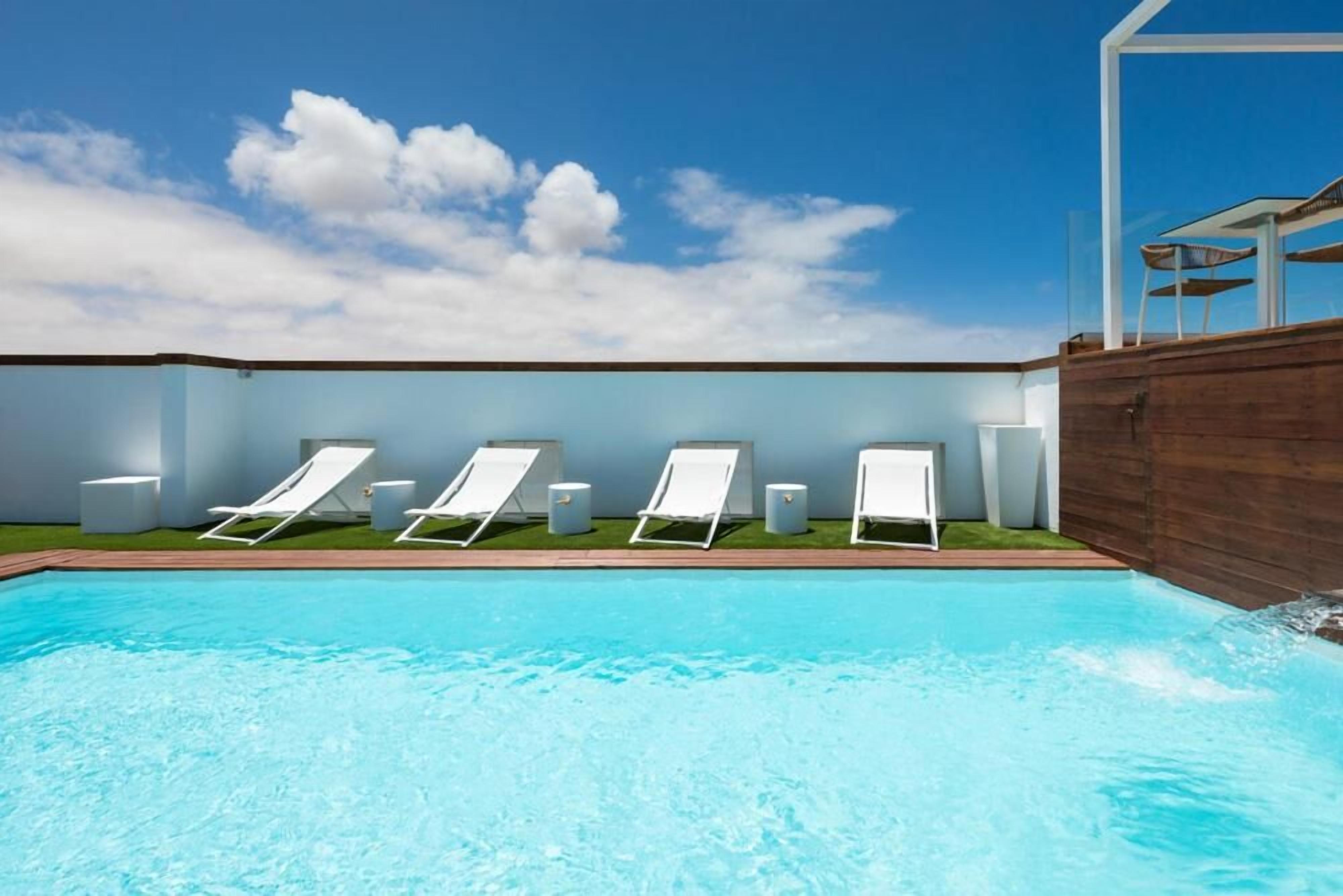 Une piscine entourée de chaises longues blanches et d’une terrasse en bois.