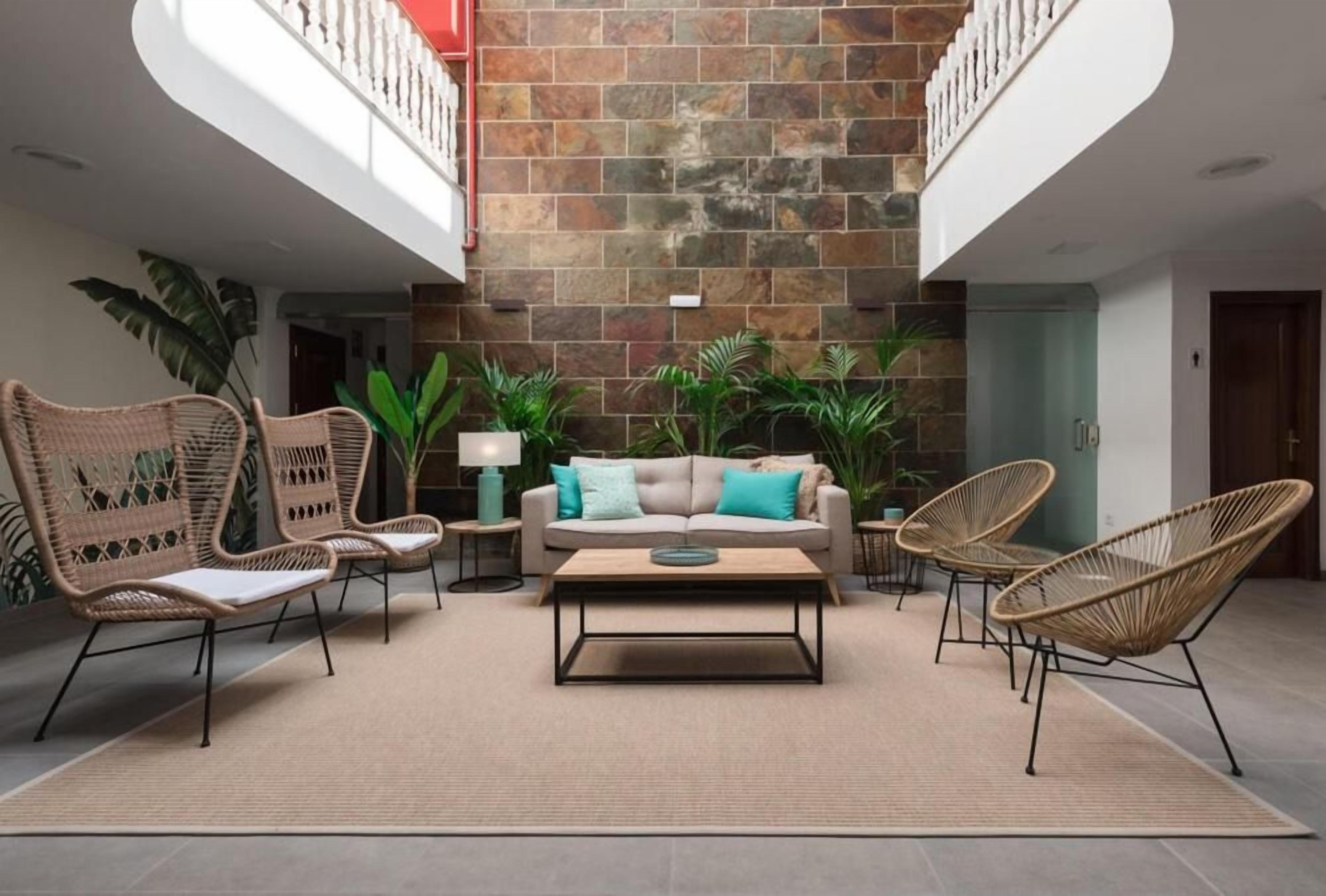 Un espacio interior amplio con pared de piedra, un sofá, dos sillones de mimbre, una mesa de centro y una lámpara.