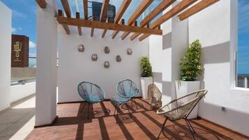 Un espacio al aire libre cubierto con vigas de madera, dos sillas azules, una silla de mimbre y decoración en la pared.
