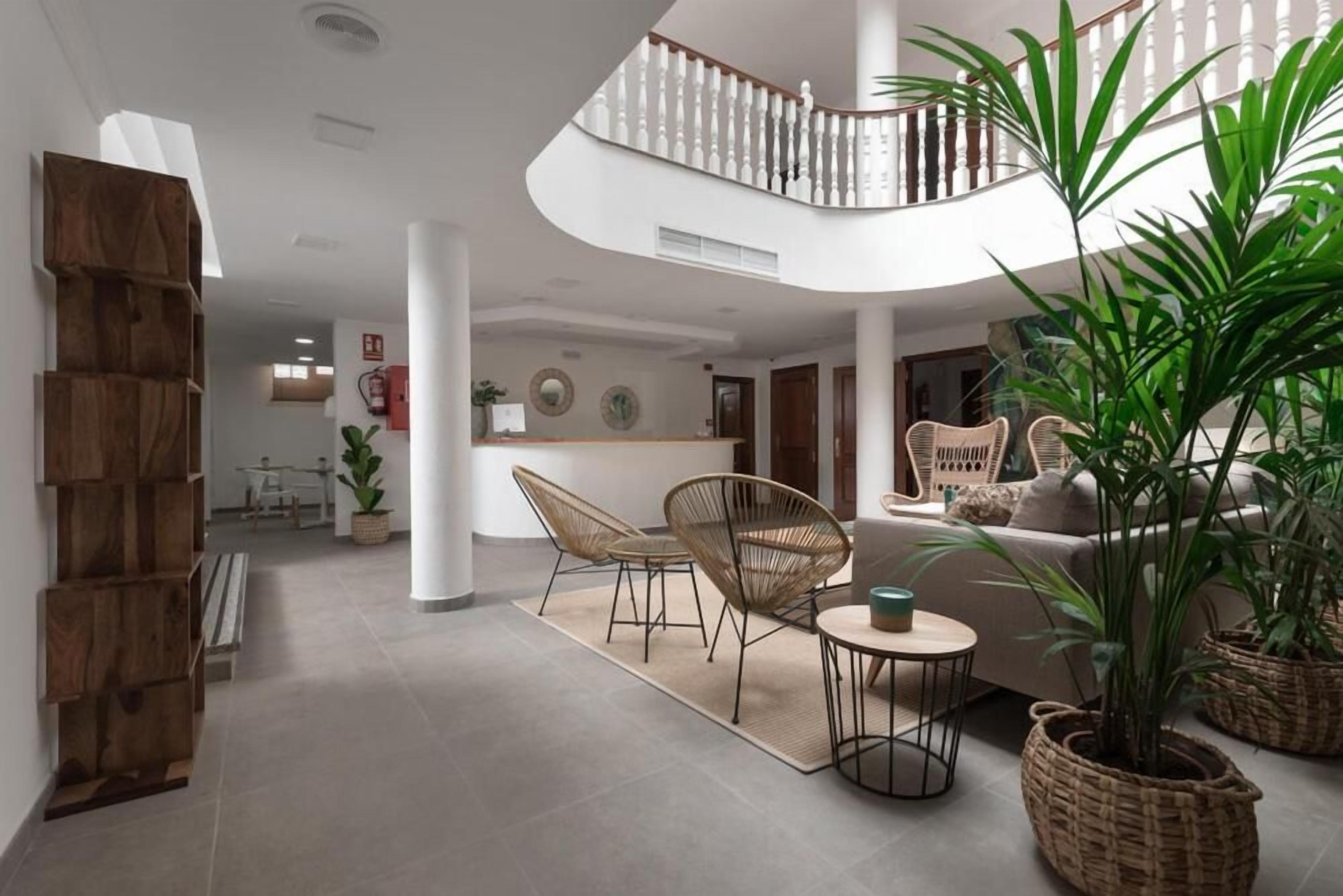 Un amplio salón con una escalera curva, mobiliario de mimbre y plantas en macetas.