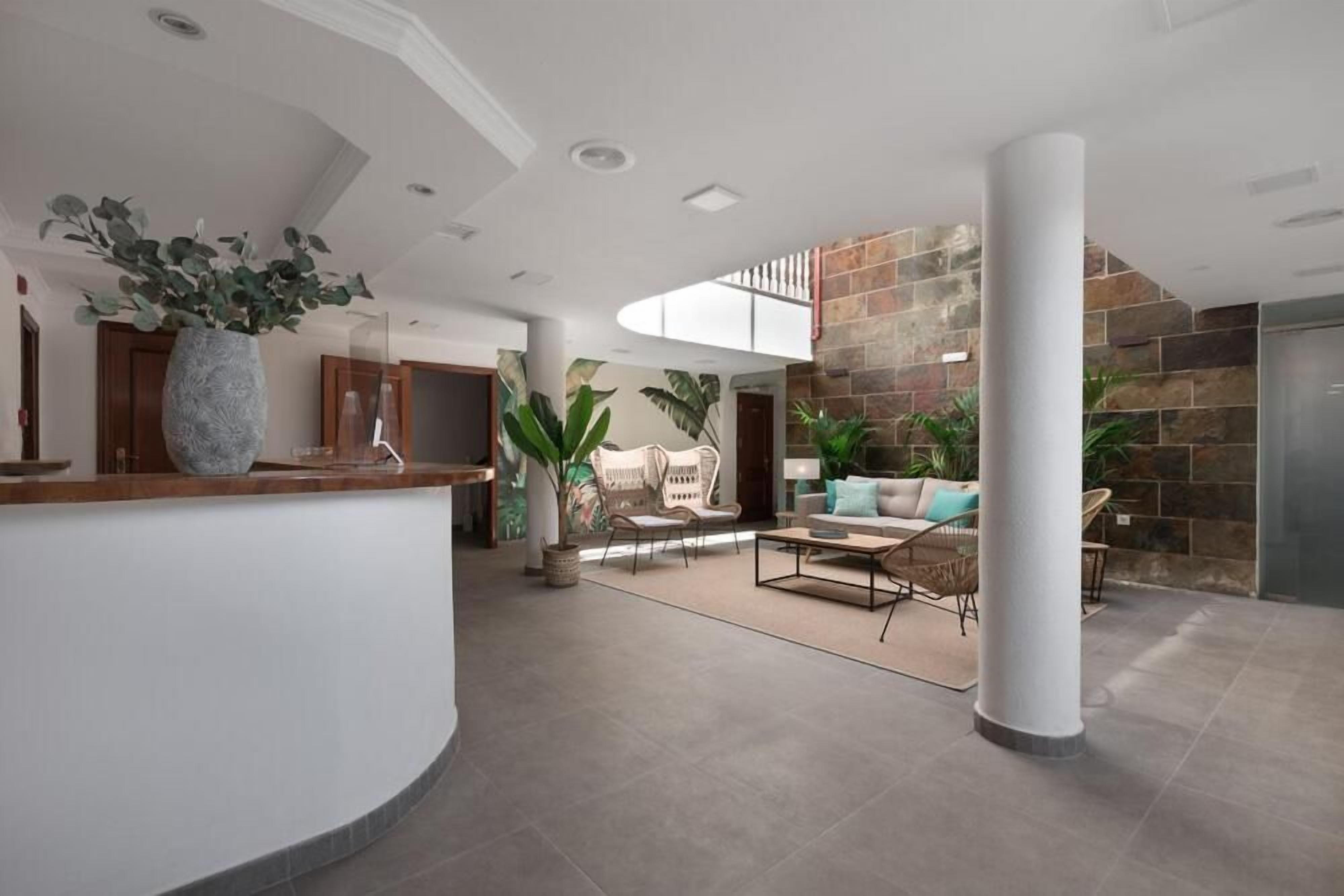 A spacious lobby with a curved reception desk, seating area with sofas and chairs, a large pillar, and a stone wall.