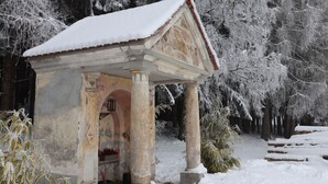 Un pabellón cubierto de nieve con techo de tejas, sostenido por columnas, en una zona boscosa.