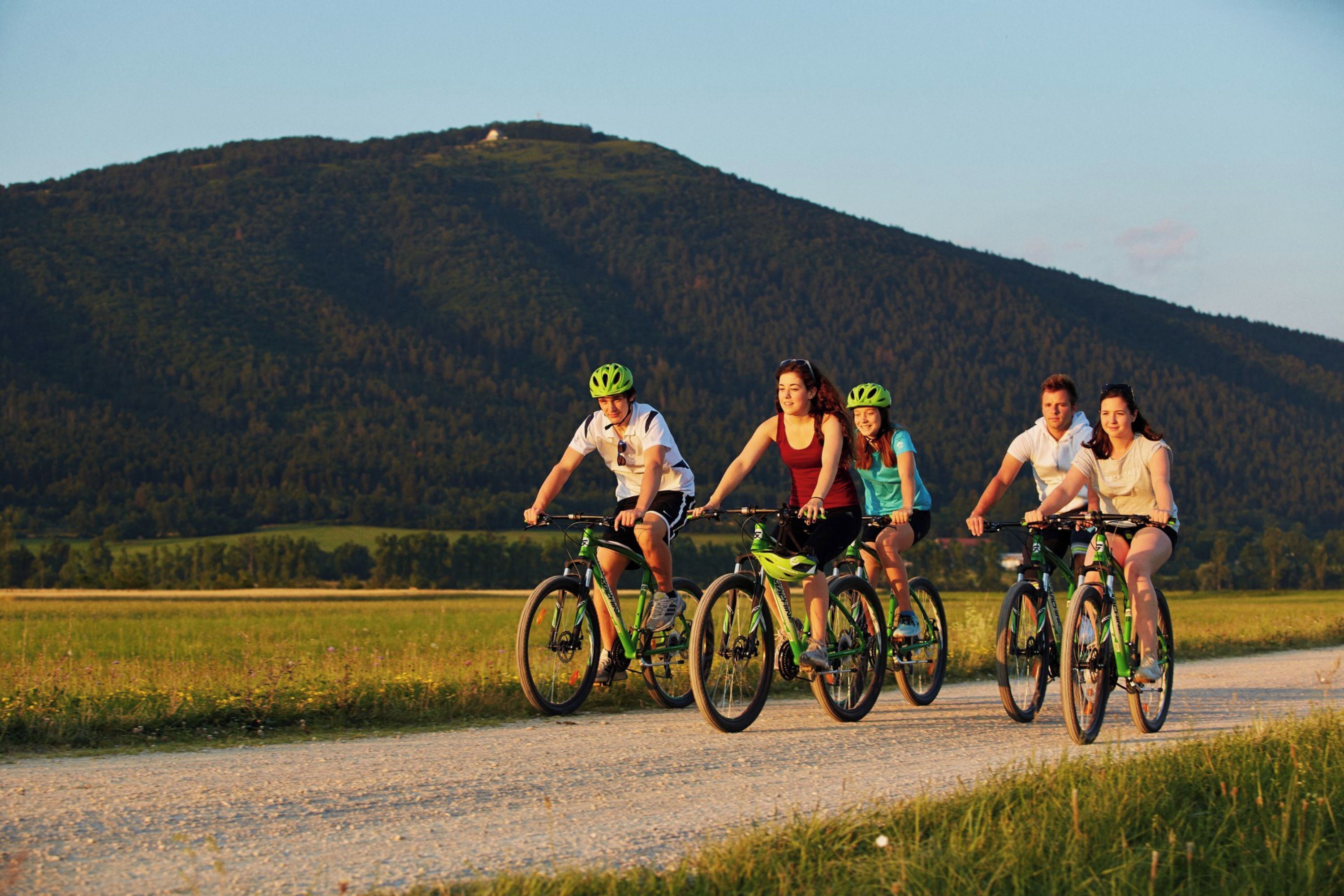 En gruppe cyklister på en grussti med en skovklædt bakke i baggrunden.
