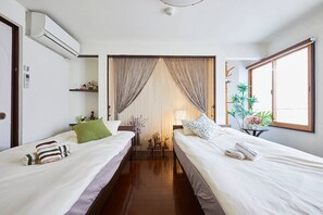 Hotellihuone, jossa on kaksi sänkyä, ikkuna, kasvi ja ilmastointilaite.