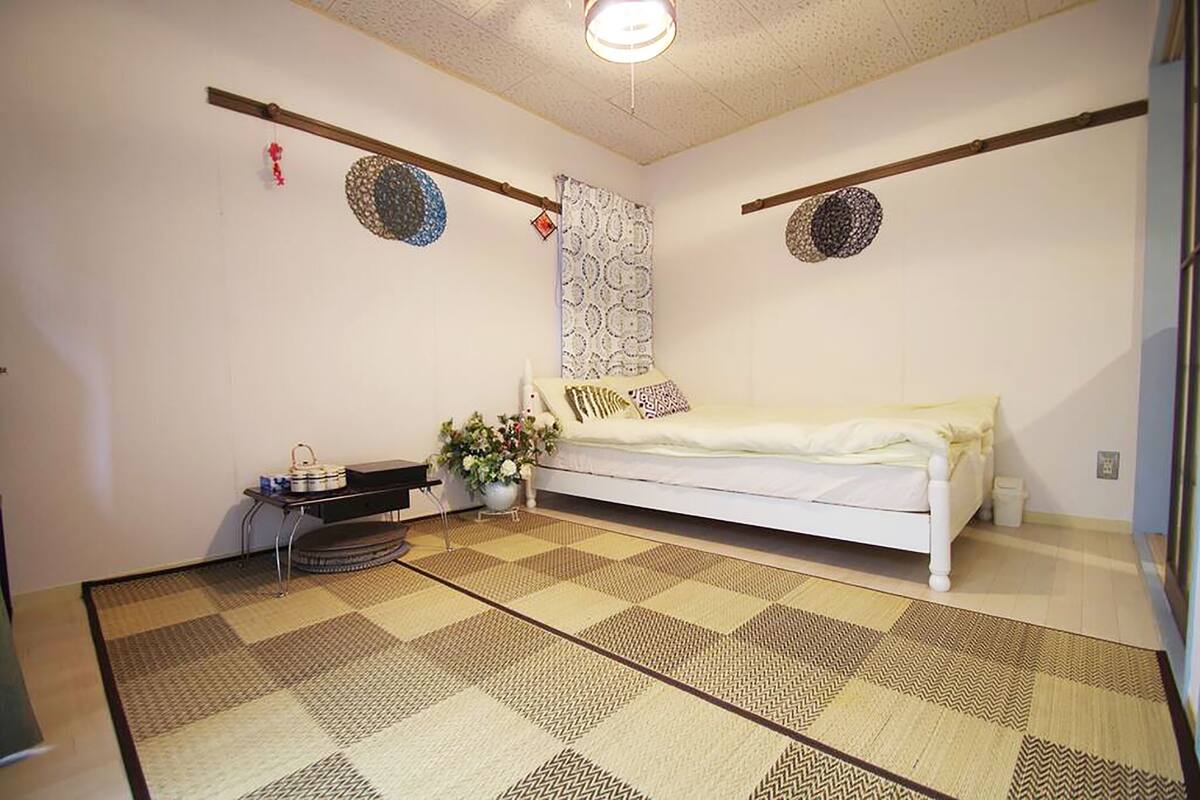 A room with a bed, a small table with a plant, and a patterned floor.