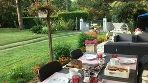 Un área de comedor al aire libre con una mesa preparada para dos personas, rodeada de follaje y un seto.