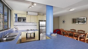 Una cocina compacta con encimera azul, electrodomésticos de acero inoxidable y un comedor con sillas de madera y una mesa.