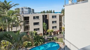 Un edificio residencial de varios pisos con balcones, piscina y palmeras alrededor.