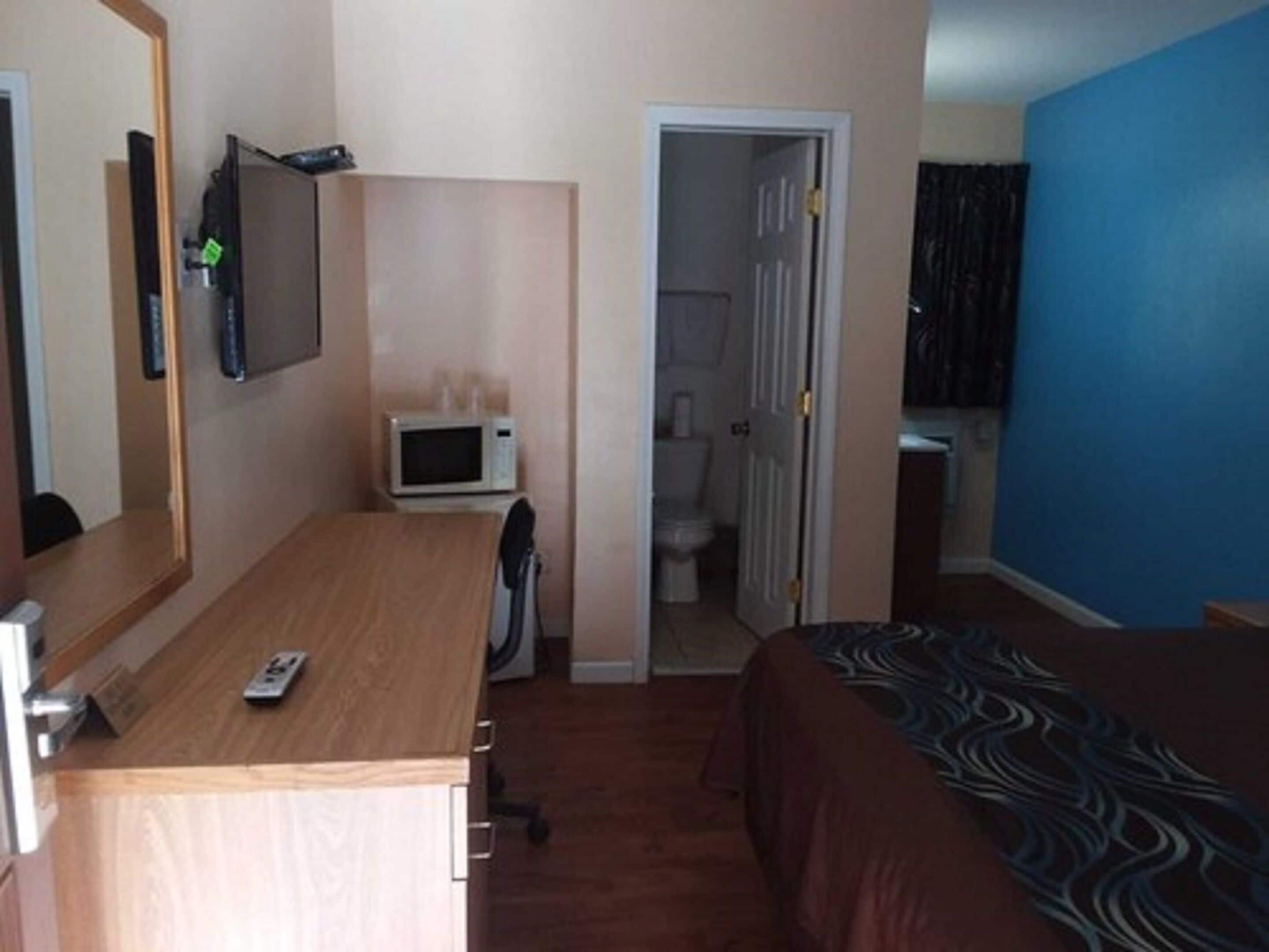 A hotel room with a wooden desk, a microwave, a bed with a patterned bedspread, a mirror, and a door leading to a bathroom.