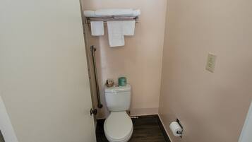Un baño pequeño con inodoro, un perchero con toallas, dispensador de papel higiénico y piso de madera.