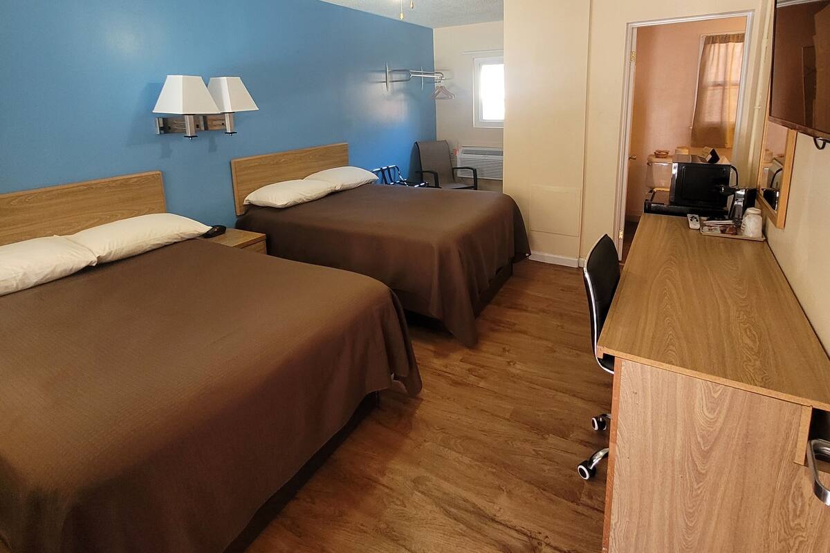 A hotel room with two beds, a desk, a chair, a ceiling fan, and a window.