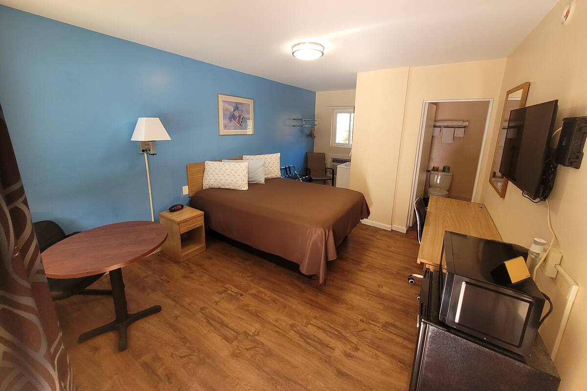 A hotel room with a bed, a desk, a chair, a TV, and a small table.