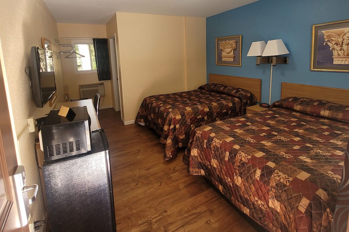 A hotel room with two beds, a desk, a refrigerator, a TV, and a window.