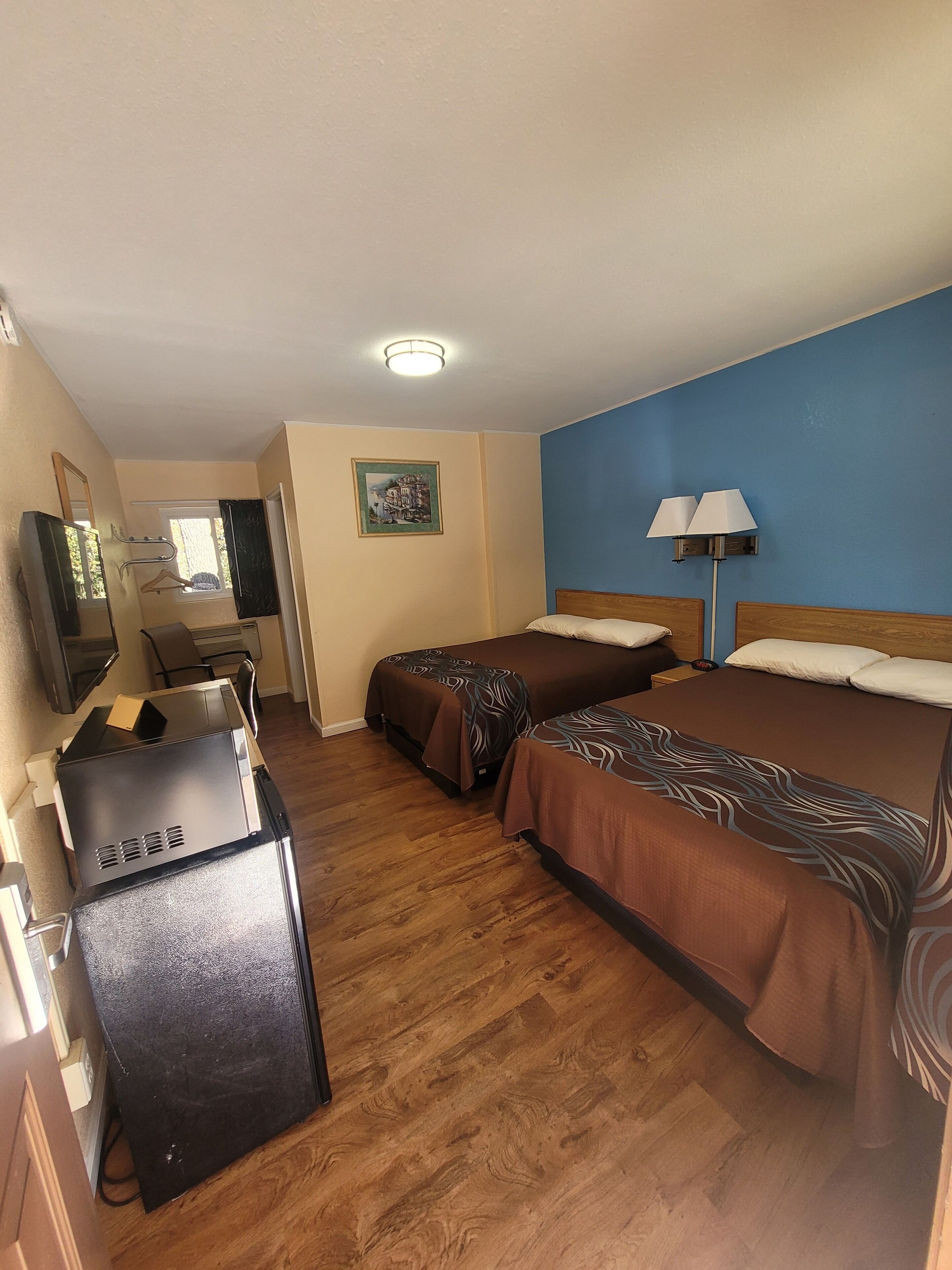 A hotel room with two beds, a desk with a computer, a TV, and a lamp.