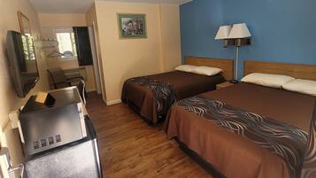 A hotel room with two beds, a desk with a computer, a TV, and a lamp.