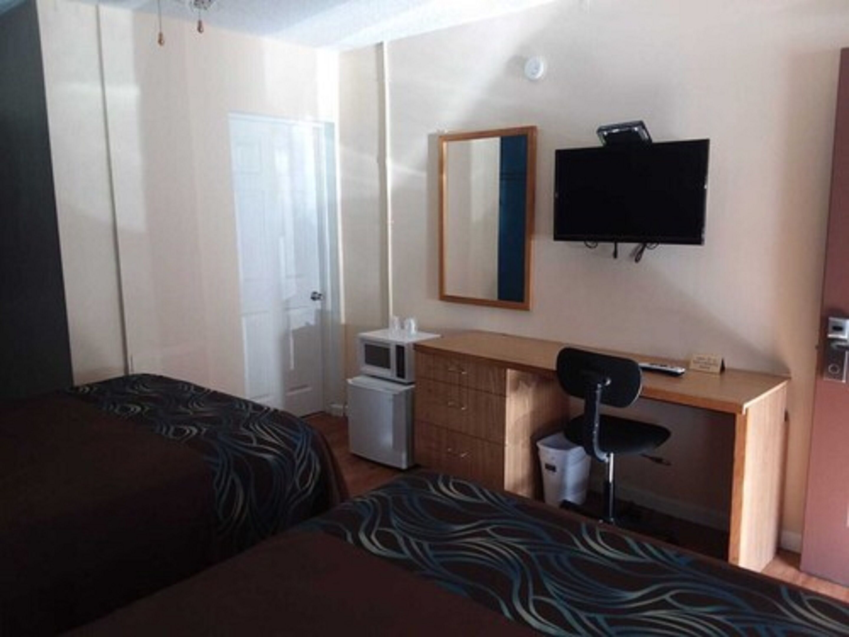 A hotel room with two beds, a desk, a chair, a television, and a small refrigerator.