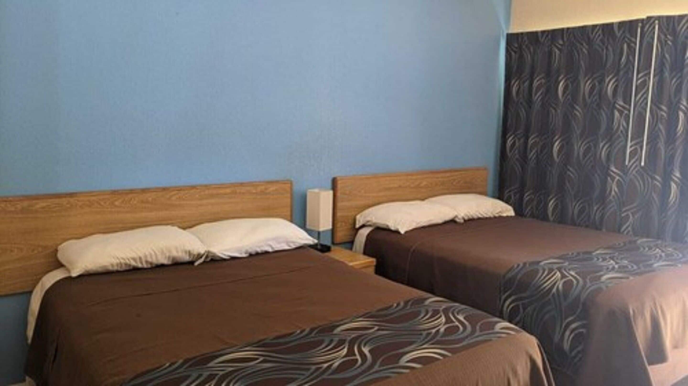 Habitación de hotel con dos camas, cabeceros de madera y una cortina estampada.