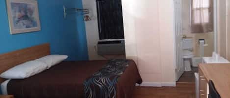 Una habitación con dos camas, un ventilador de techo, un cuadro en la pared y un baño visible a través de una puerta abierta.