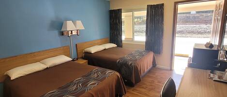 A hotel room with two beds, a desk, a lamp, and a view of the outdoors.