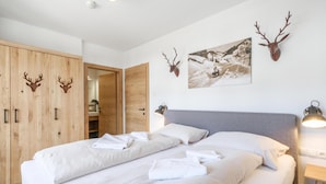 Un dormitorio con dos camas, un armario de madera con adornos de cabeza de ciervo, un cuadro de un paisaje nevado y una lámpara de noche.