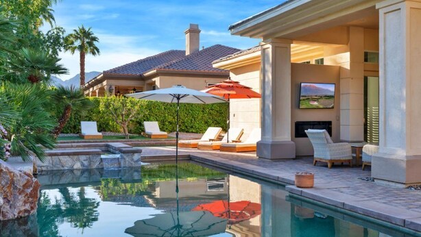 A pool area with lounge chairs and umbrellas, a fireplace, and a TV mounted on the wall.